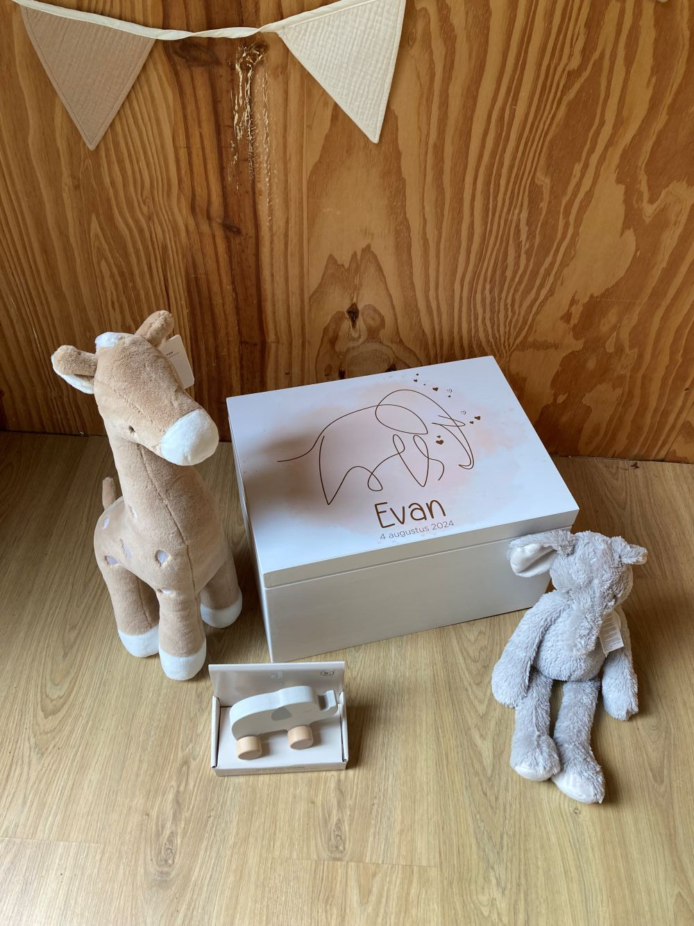 Een herinneringskist met naam in stijl van het geboortekaartje. Om de kist heen zitten knuffels en een olifant roldiertje