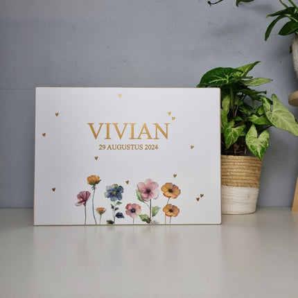 Wit houten kist met naam en datum in stijl van het geboortekaartje. Op deze kist staan mooie veldbloemen en hartjes