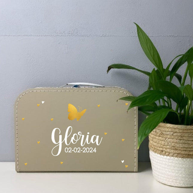 Een kinderkoffertje met naam en datum erop en er is een vlindertje bovenop