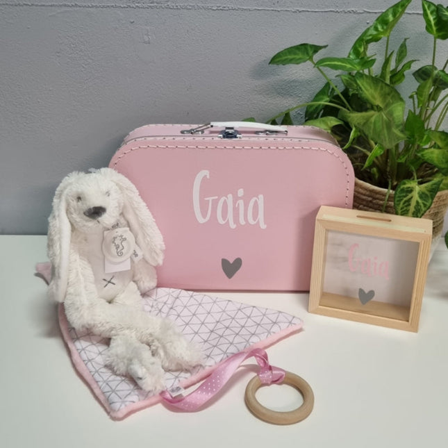 kraamcadeau pakket bestaand uit koffertje met naam en met een hartje erop daarnaast is er een witte knuffelen een houten spaarpot